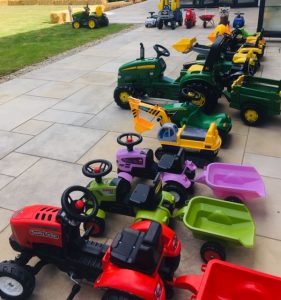 a collection of ride on toy tractors with trailers, in various colours.
